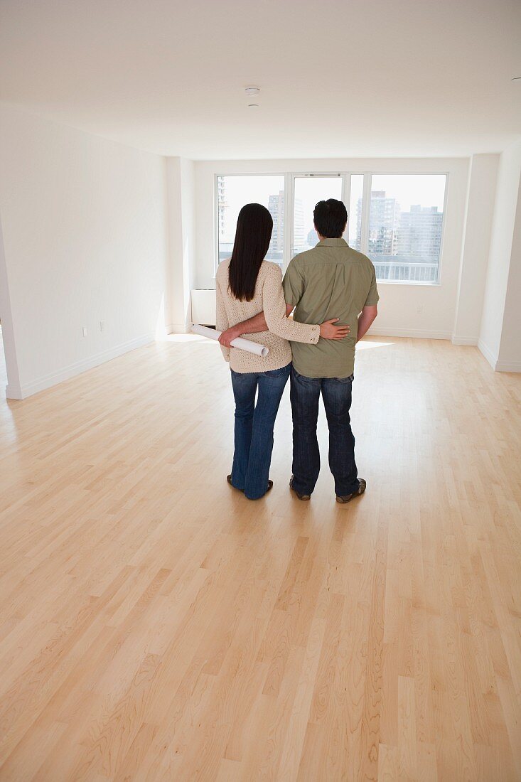 Rear view of couple with blueprints in empty room