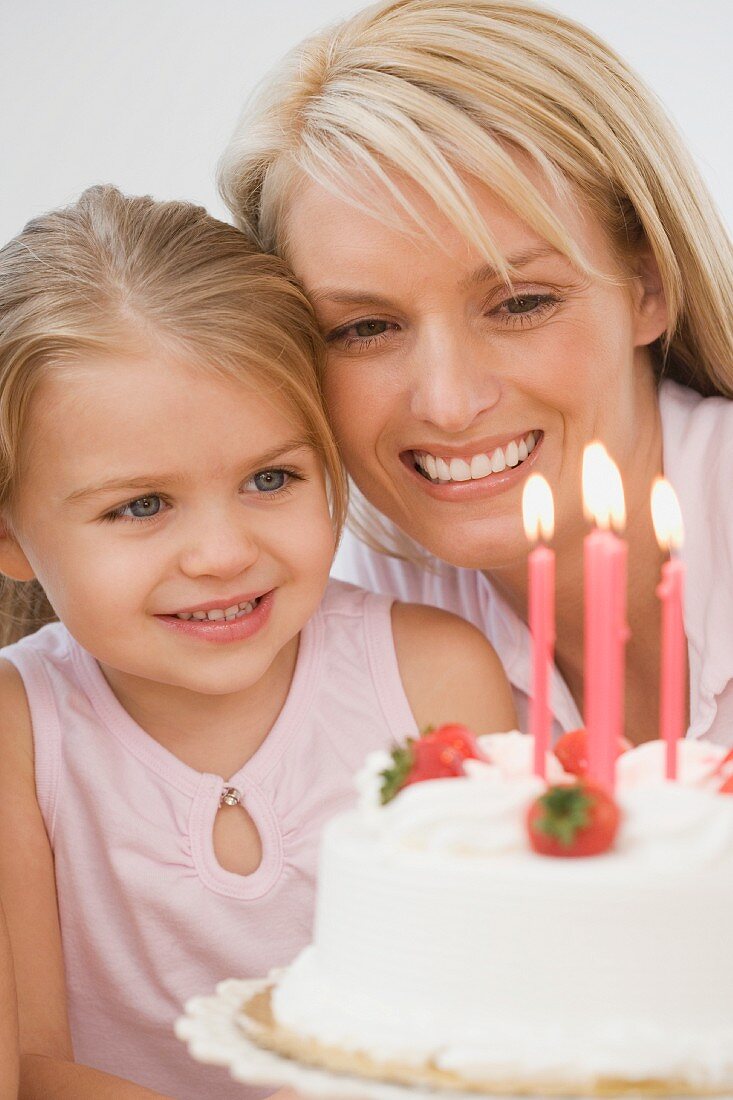 Mutter und Tochter blicken lächelnd auf Geburtstagstorte