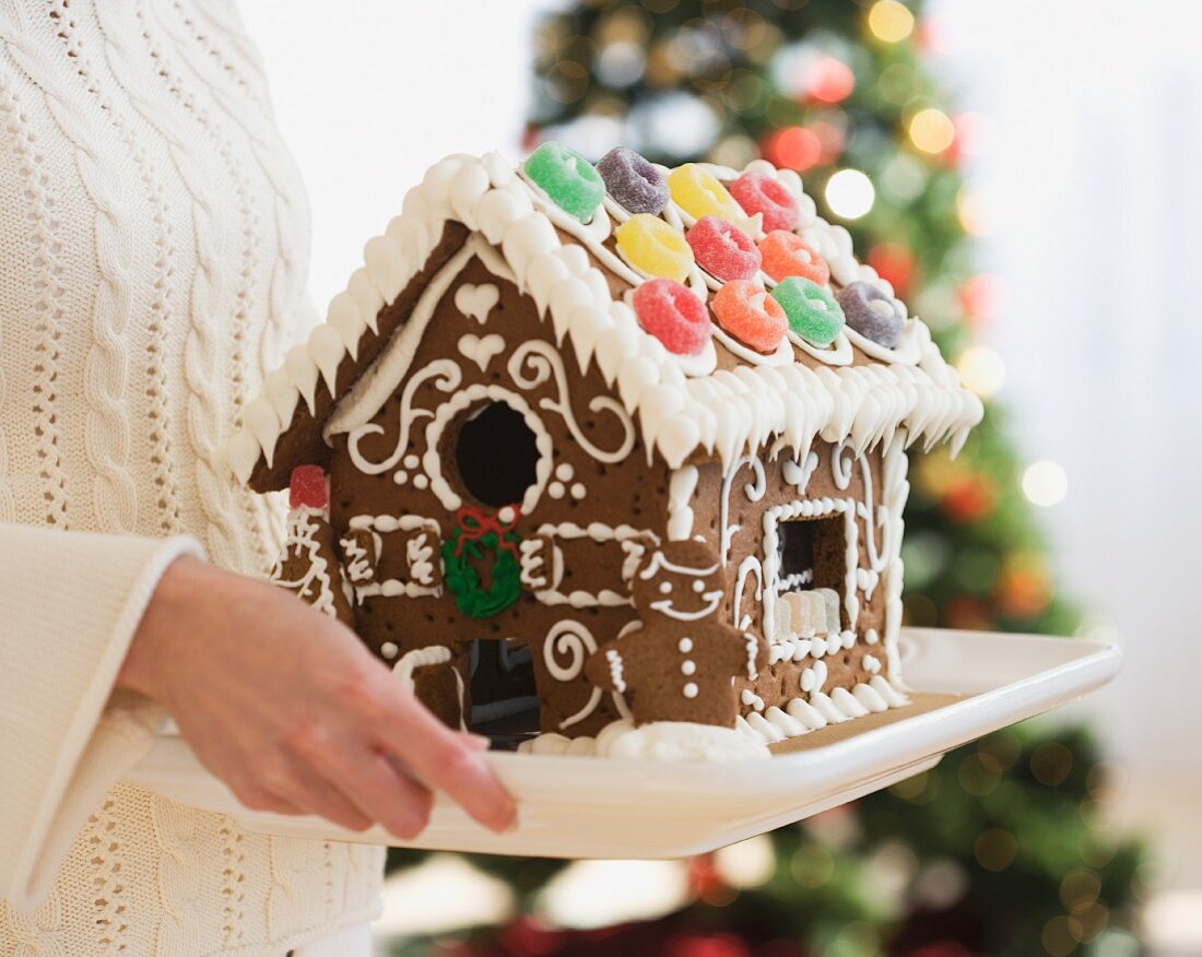 Woman holding gingerbread house on tray