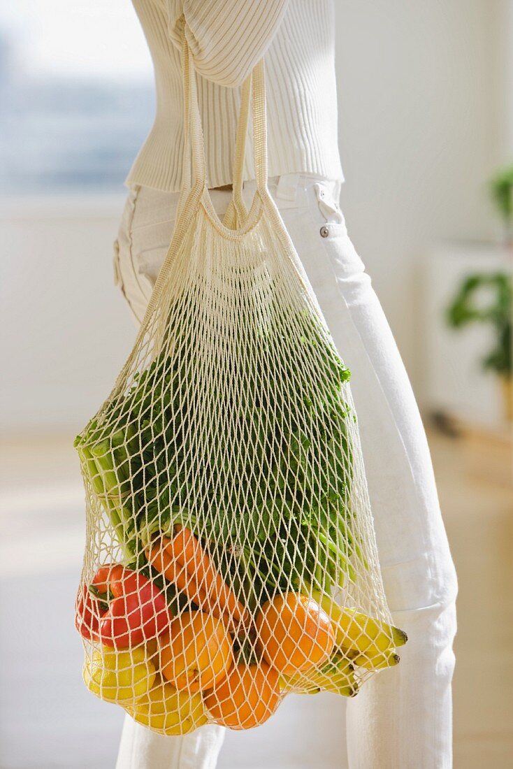Frau trägt Netz mit Obst und Gemüse