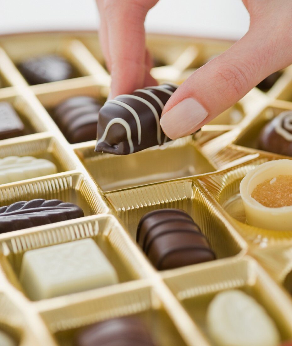 Woman holding chocolate over box of chocolates