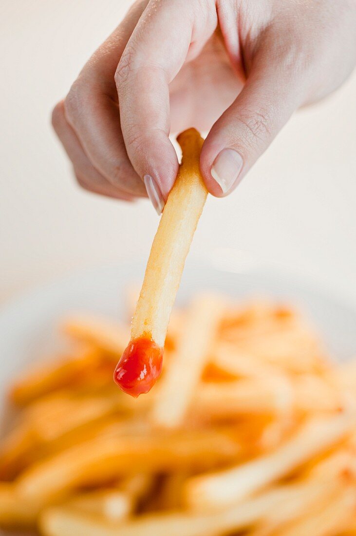 Frauenhand hält Pommes frites mit Ketchup