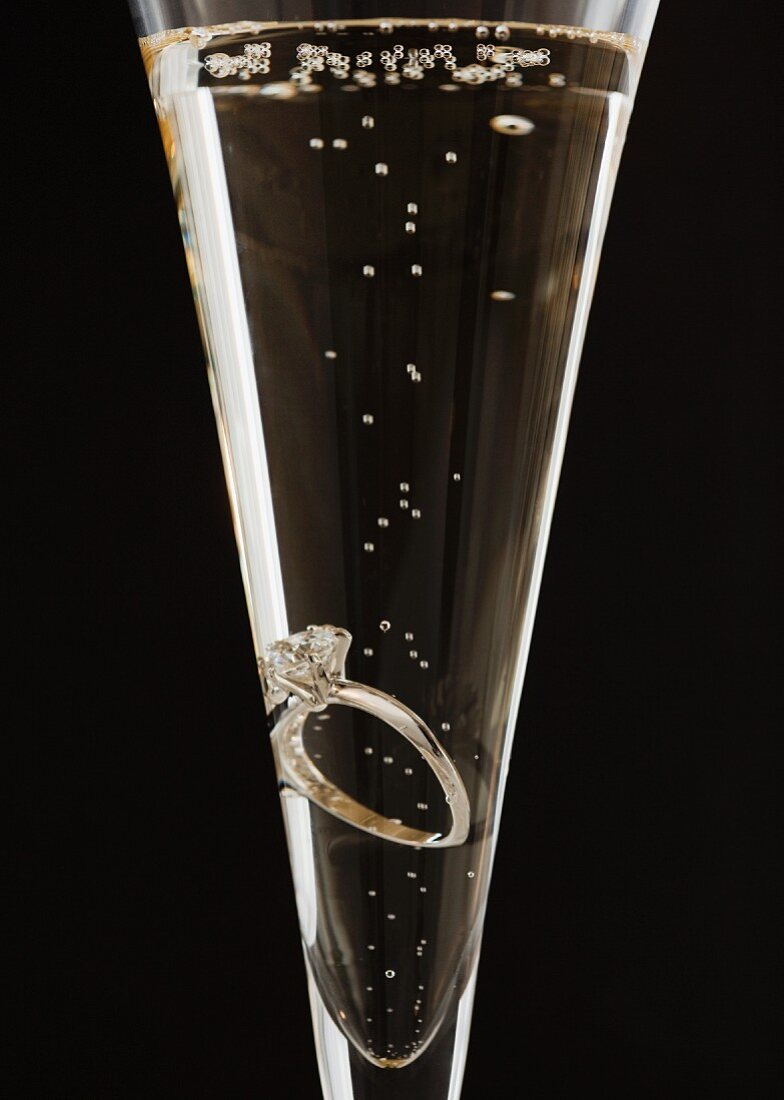 Sektglas mit Verlobungsring vor schwarzem Hintergrund