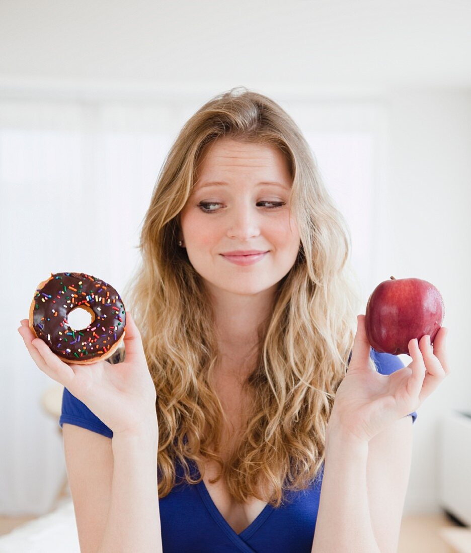 Junge Frau hat die Wahl zwischen einem Doughnut und einem Apfel