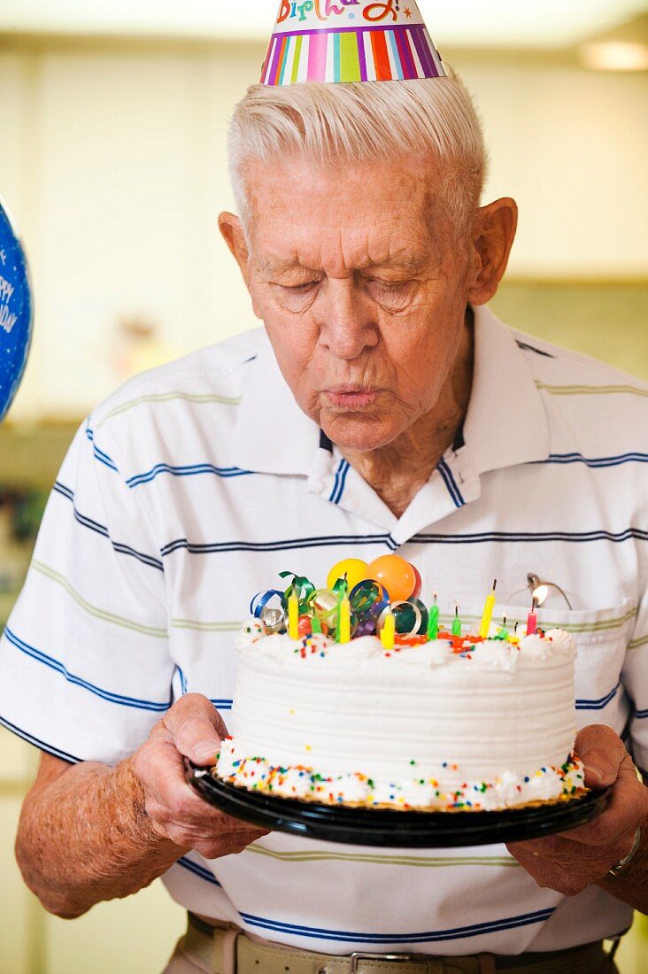 Senior man blowing candles on birthday cake