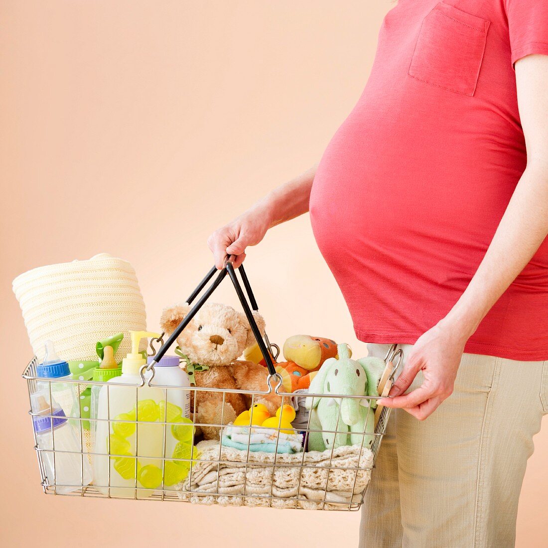 Schwangere Frau hält Einkaufskorb mit Babysachen