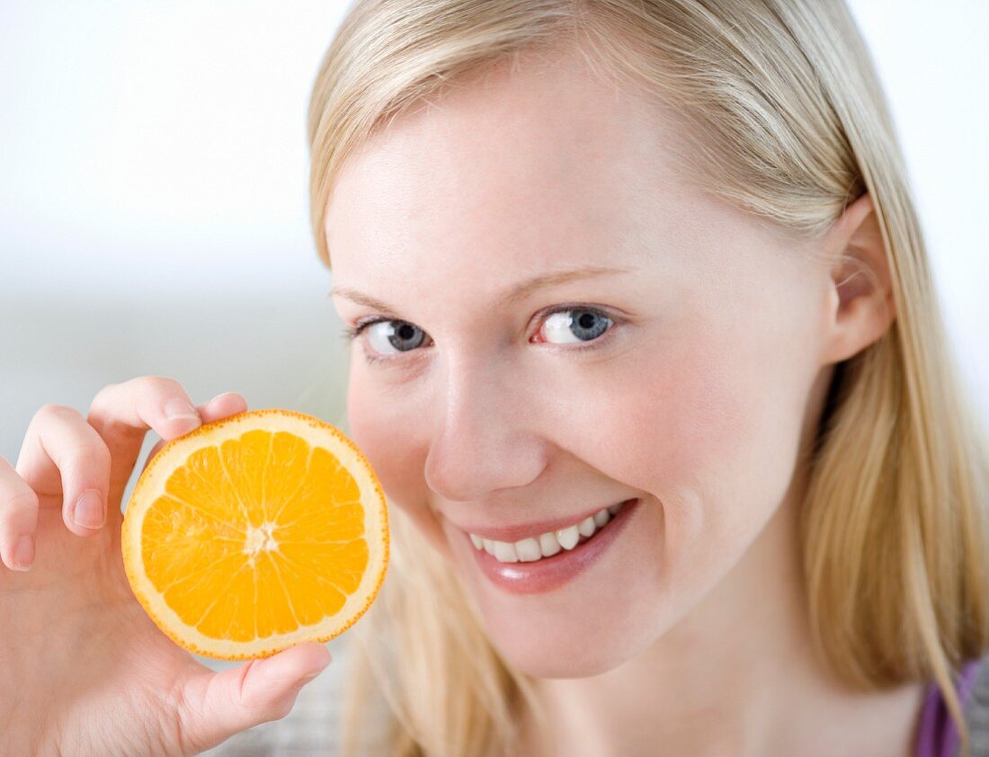 Junge Frau hält eine Orangenhälfte