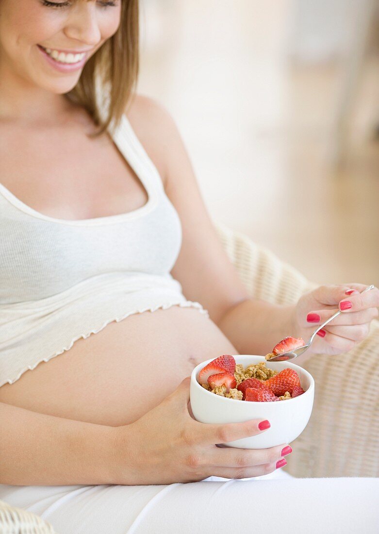 Schwangere Frau isst Müsli mit Erdbeeren