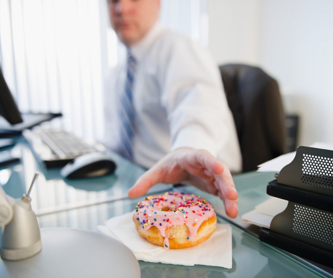 Mann im Büro greift nach Donut
