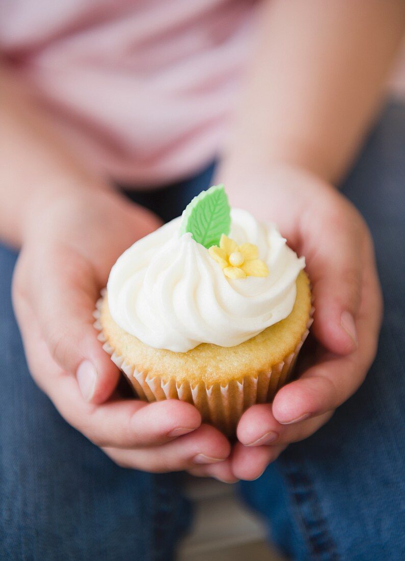 Close up of girl's (8-9) hands holding cupcake