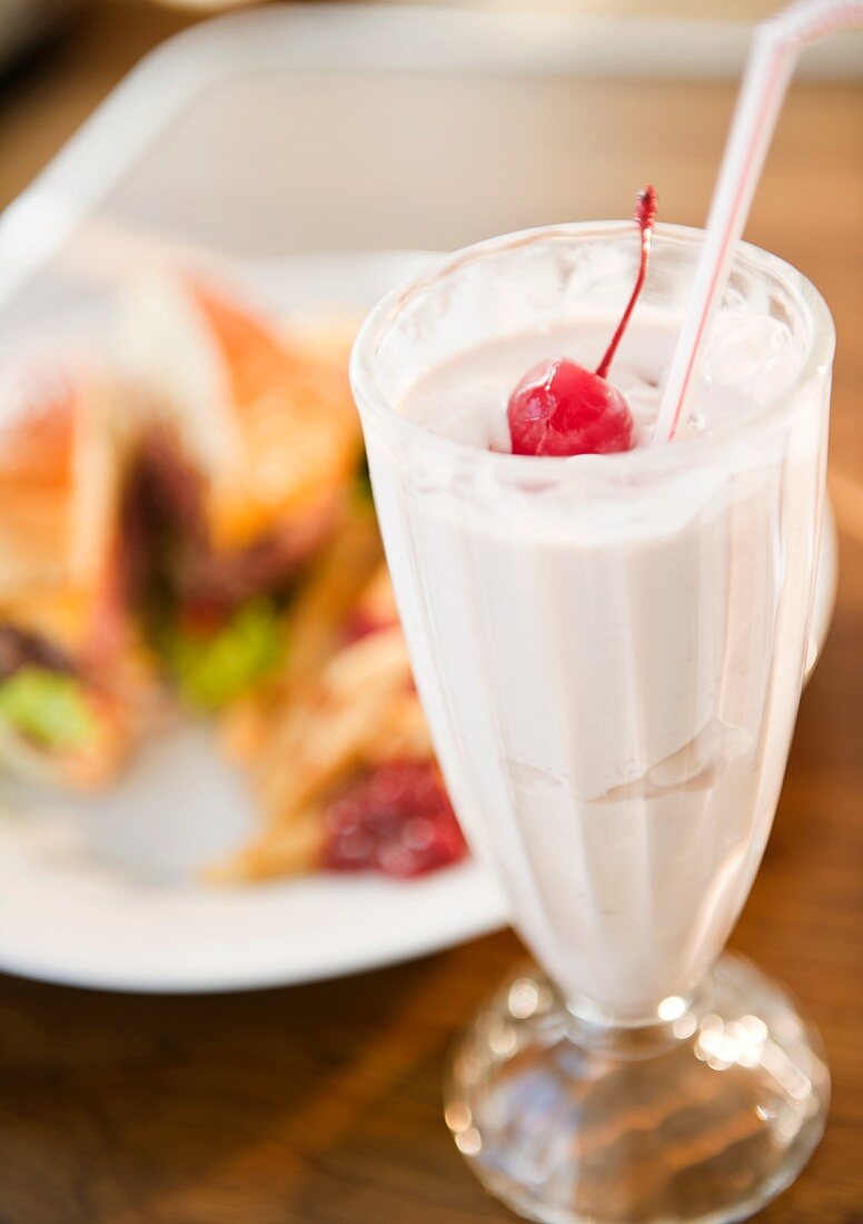 Milchshake, im Hintergrund Burger mit Pommes Frites