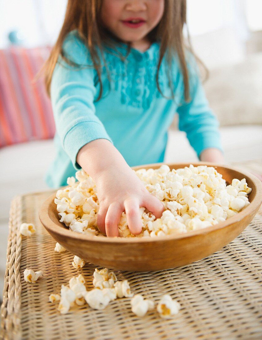 Kleines Mädchen greift in Schale mit Popcorn