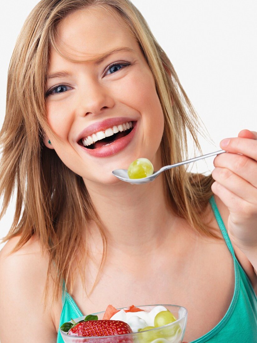 Junge Frau isst lachend einen Fruchtsalat