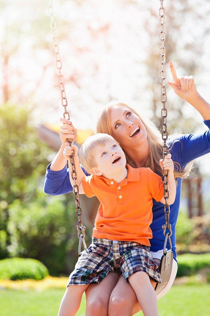 USA, Washington State, Seattle, Mother and son (2-3) swinging on swing in park