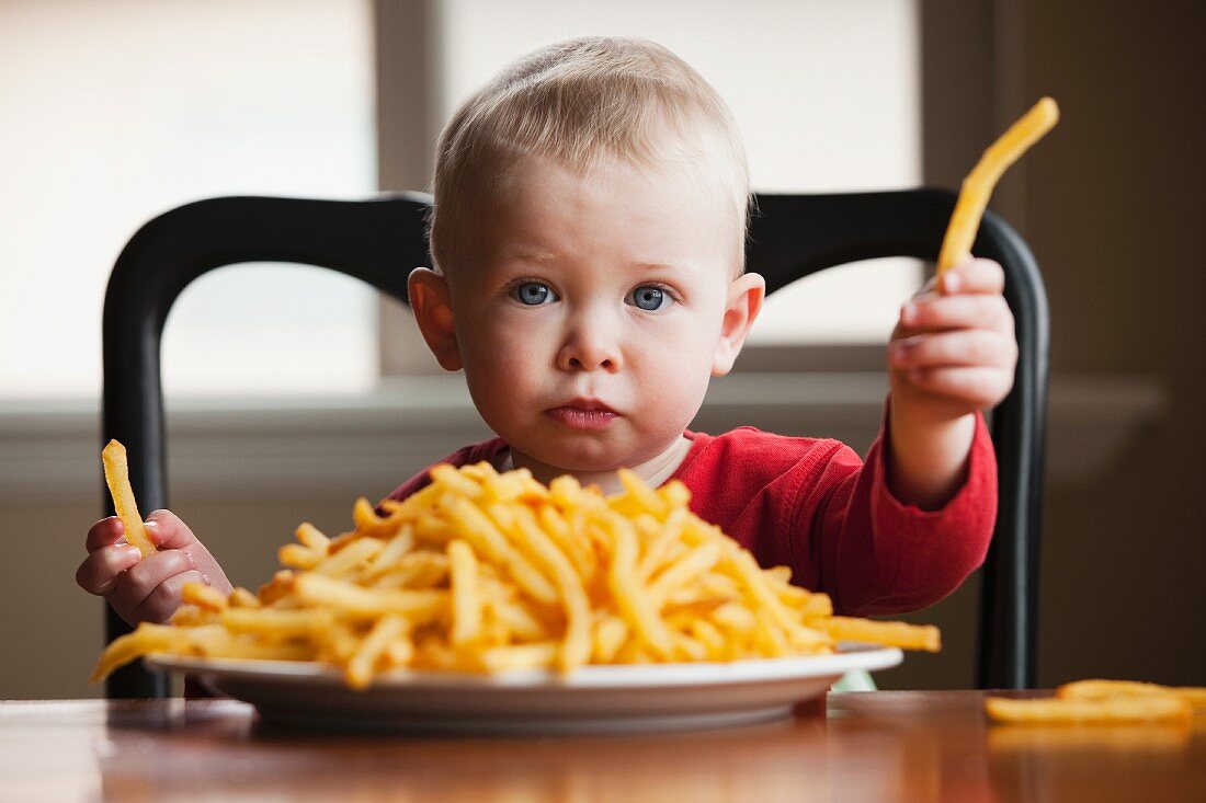 Kleiner Junge hinter einem großen Teller mit Pommes Frites