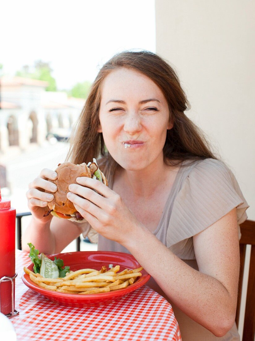 Junge Frau isst Burger mit Pommes frites