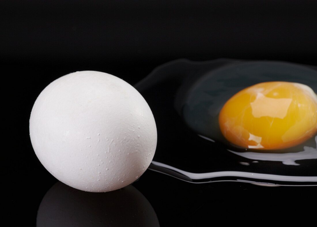 Ganzes und aufgeschlagenes Ei auf schwarzem Hintergrund