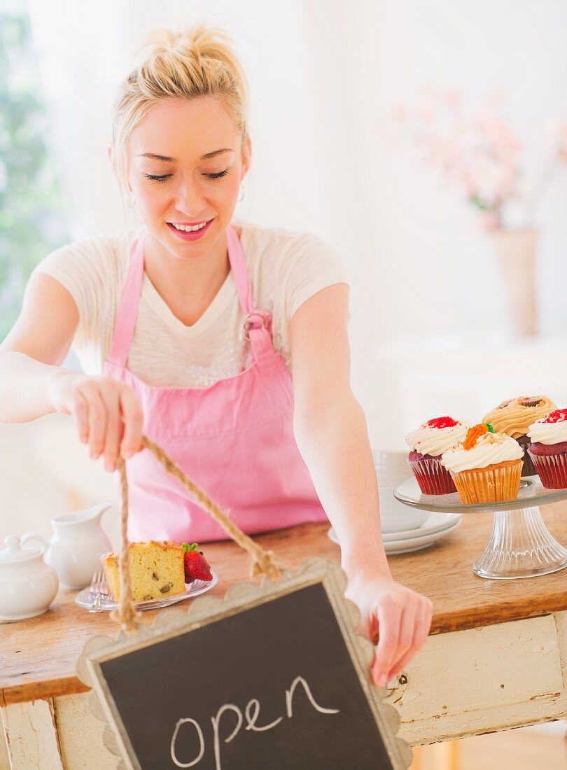 Smiling young woman in apron holding open sign