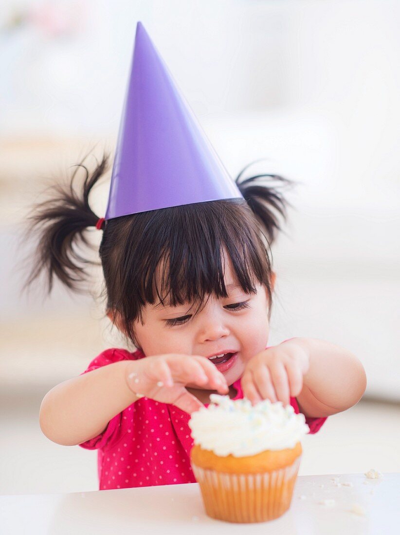 Baby mit Partyhut isst Cupcake