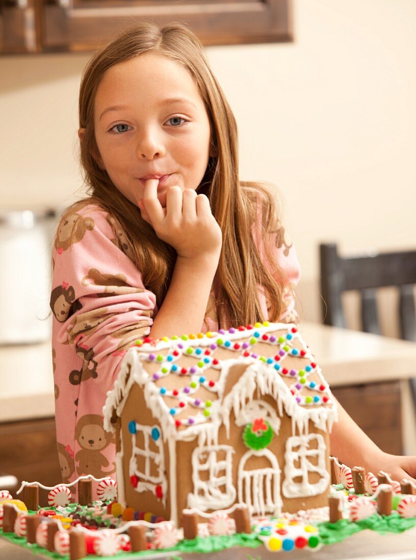 Portrait of girl (6-7) licking finger by gingerbread house