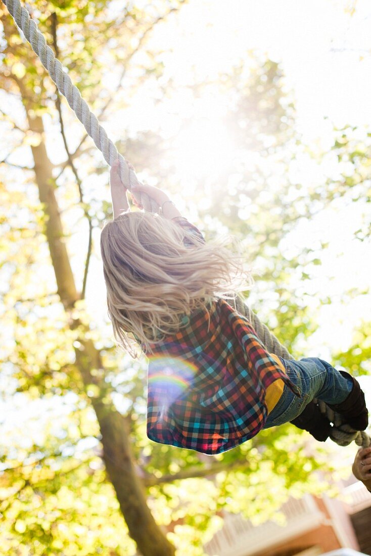 Blondes Mädchen hängt an einem Seil im Garten