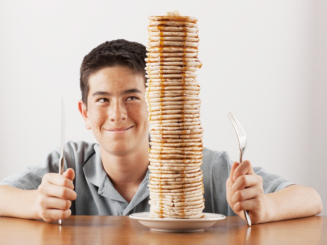 Junge sitzt hinter einem hohen Stapel Pancakes
