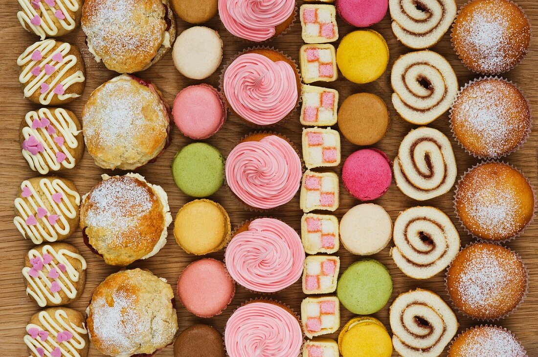Reihen von Cupcakes, Scones, Macarons, Biskuitrolle und Stücke von Mini Battenburg Cake
