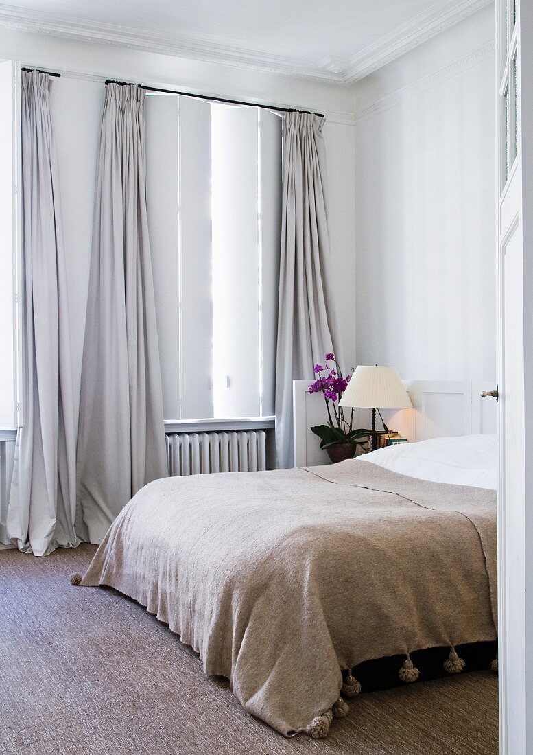 View through open door of double bed next to window with floor-length curtains