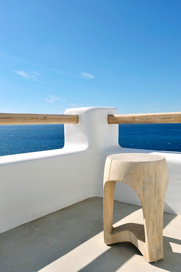 Holzschemel in Ecke einer Dachterrasse unter blauem Himmel mit Blick auf das Meer