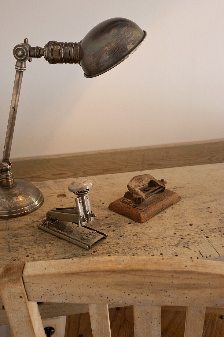 Silver desk lamp, hole punch and stapler on worm-eaten wooden table