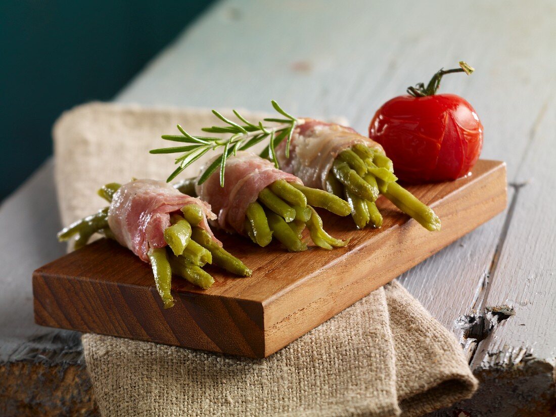 Green beans wrapped in bacon with rosemary on a small wooden board
