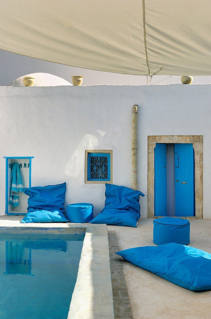 North-African-style courtyard with blue floor cushions and pouffes around pool