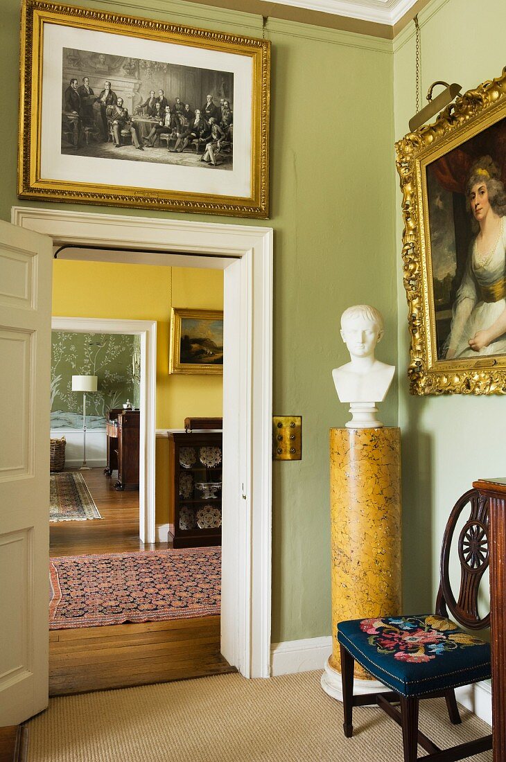 Gilt-framed paintings and bust of a man on marble pedestal; view through suite of rooms in English manor house