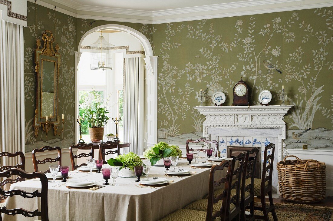 Festively set table, mantle clock and floral wallpaper in dining room of English country house