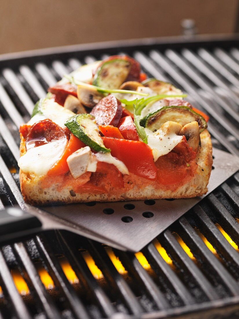 A slice of sausage, vegetable and mozzarella pizza cooked on the barbecue, on a spatula