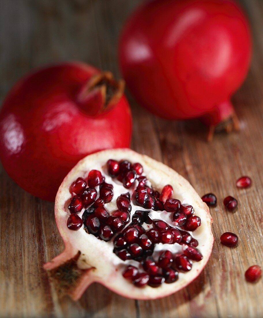 Leuchtend rote Granatäpfel; im Vordergrund eine Granatapfelhälfte