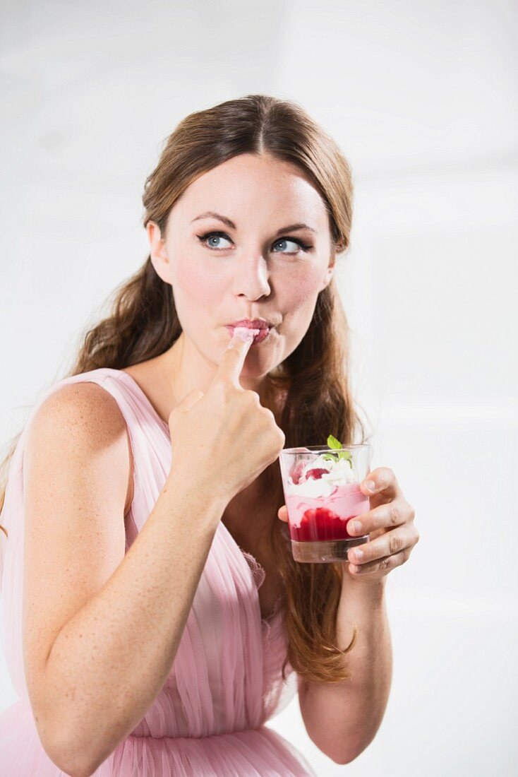 Germany, Young woman with glass of yogurt, licking finger