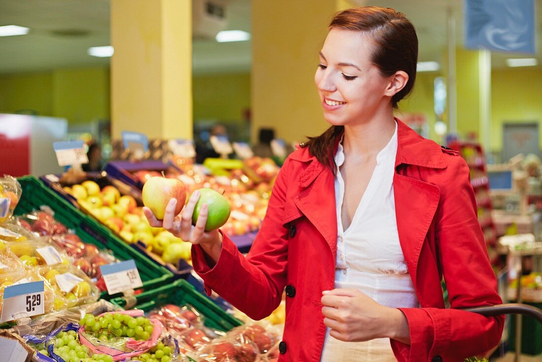 Junge Frau vergleicht Äpfel im Supermarkt