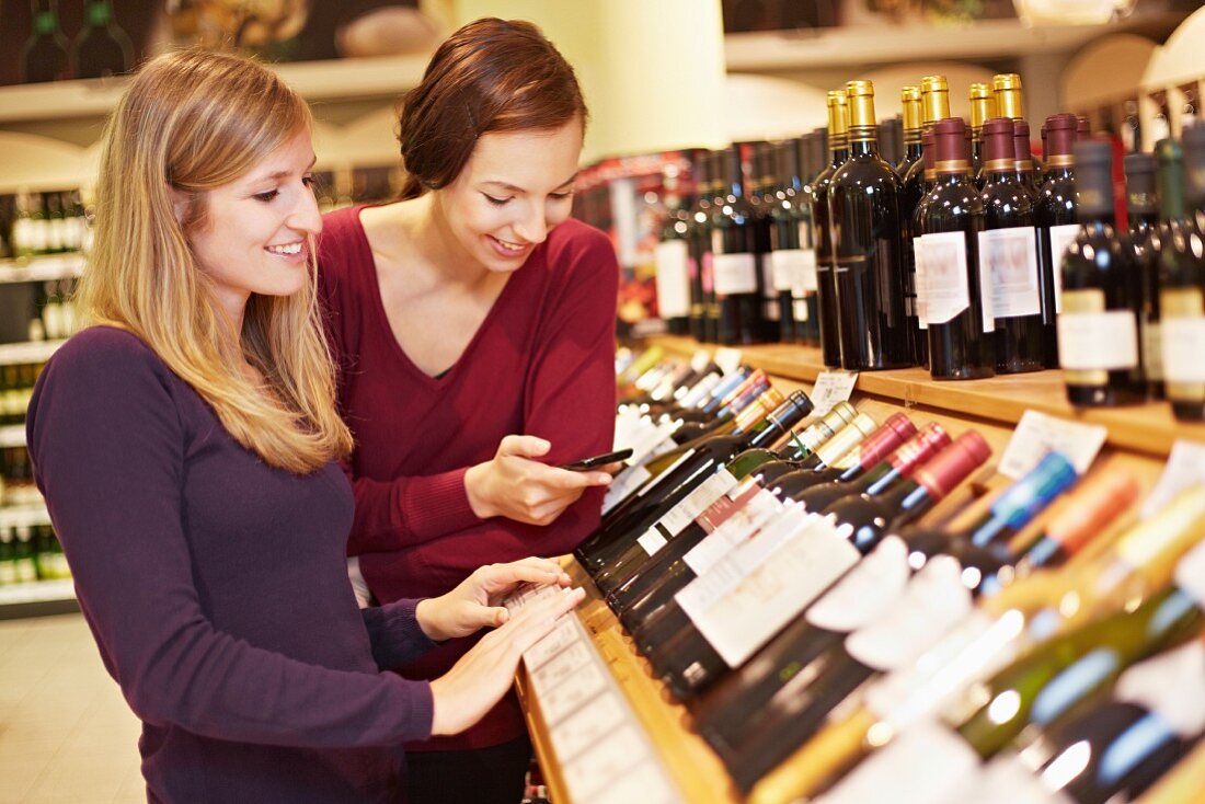 Junge Frauen prüfen Weinflaschen im Supermarkt