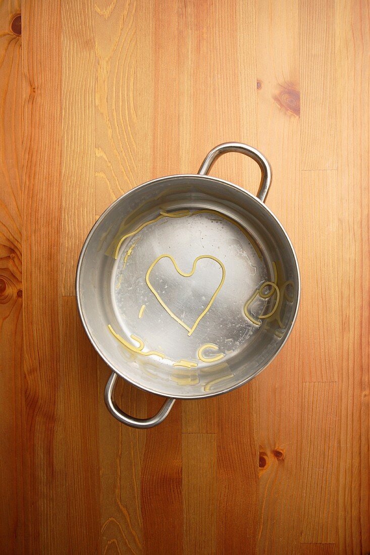Heart shaped spaghetti in cooking pot on wooden table