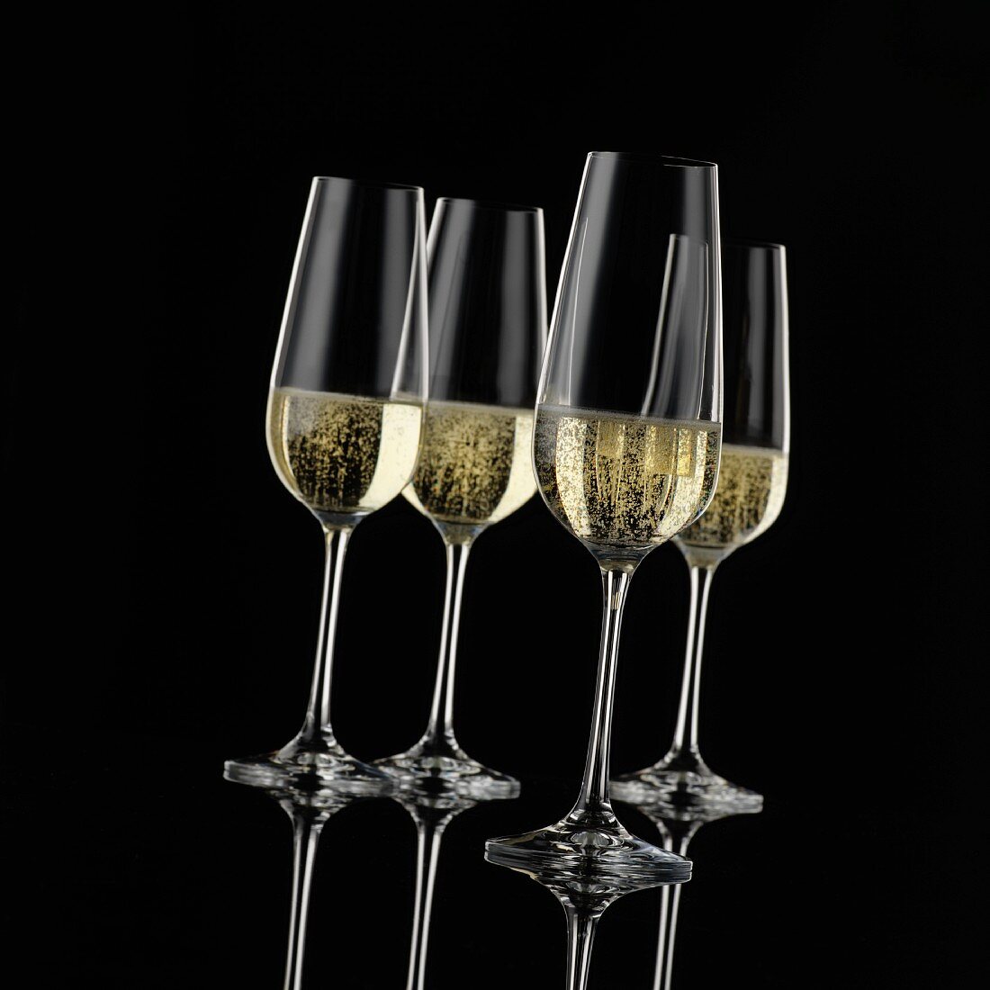Four champagne glasses in front of a black background