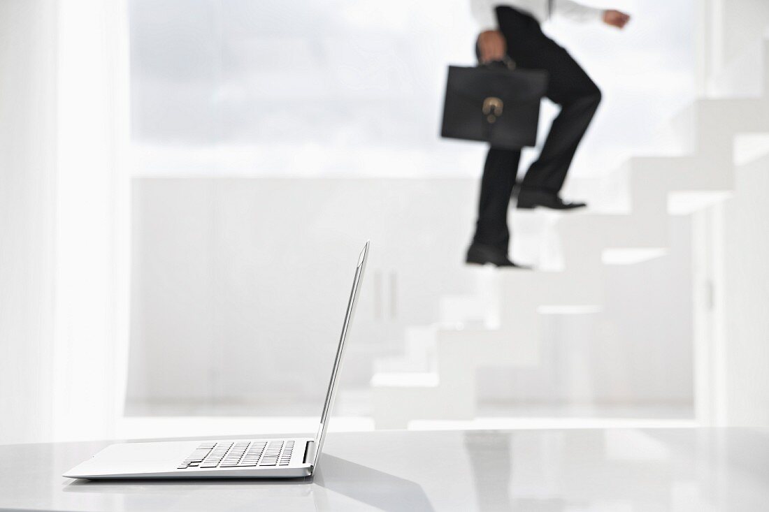 Spain, Businessman cimbing up stairs, laptop in foreground