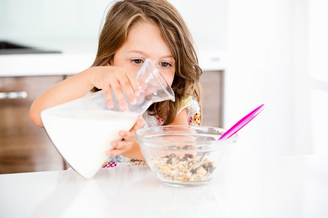 Germany, Girl pouring milk in muesli