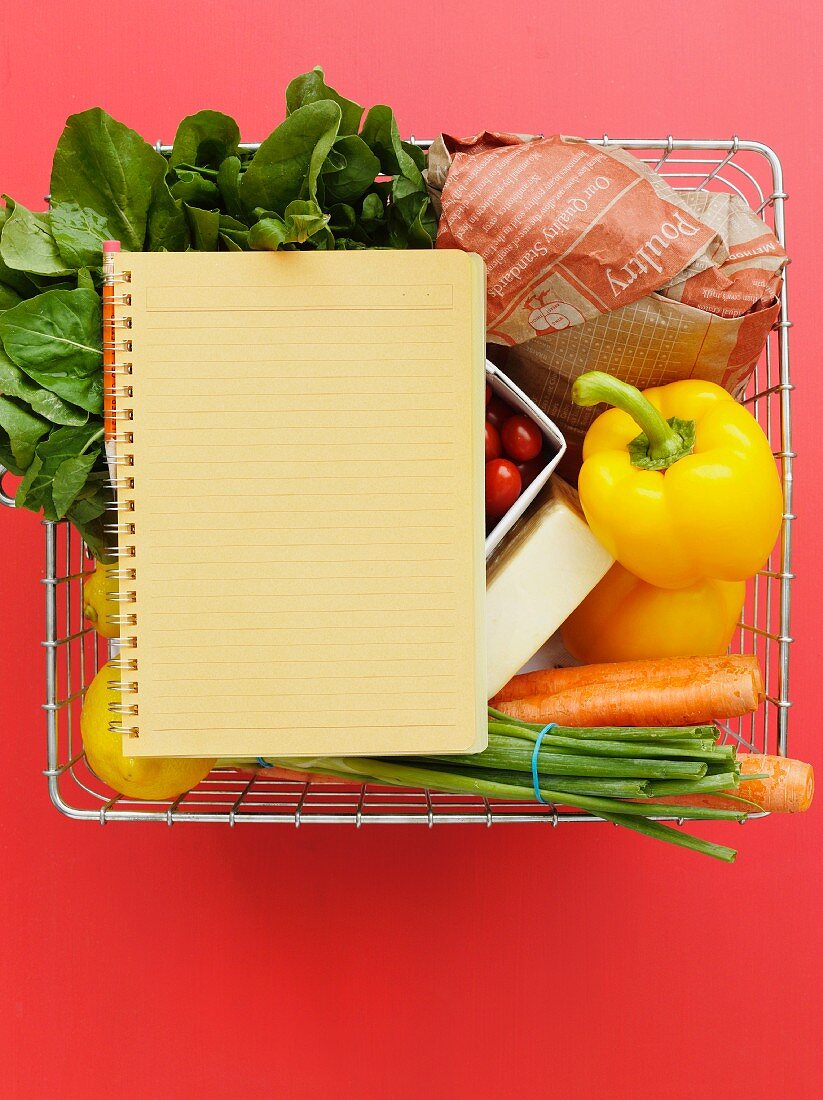 A shopping basket with vegetables, lemons and a notebook