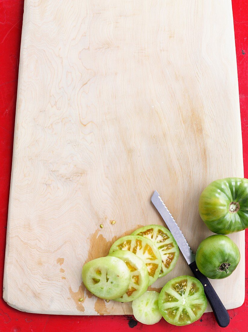 Green tomatoes, partly sliced, on a chopping board