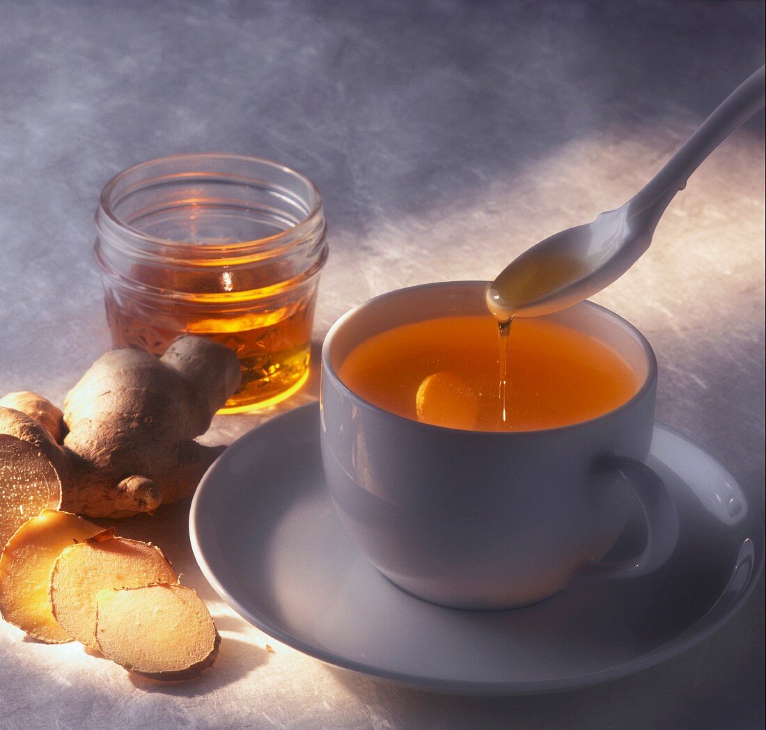 Spooning Honey into a Cup of Ginger Tea; Sliced Ginger