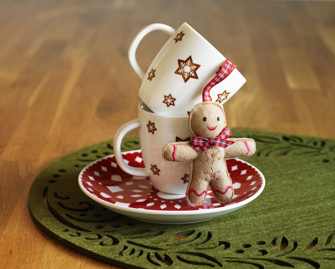 Two Christmas Mugs Stacked on a Saucer with a Small Stuffed Gingerbread Man