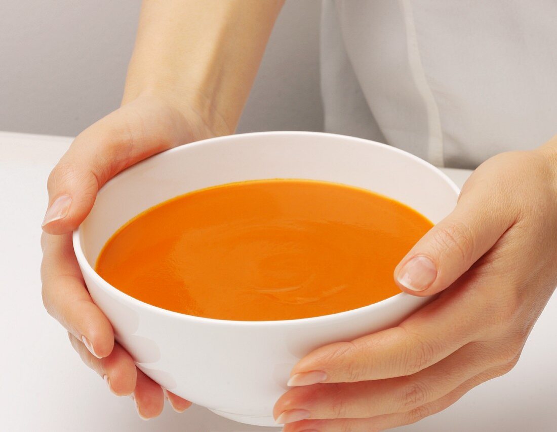 Frauenhände halten eine Schüssel Tomatencremesuppe