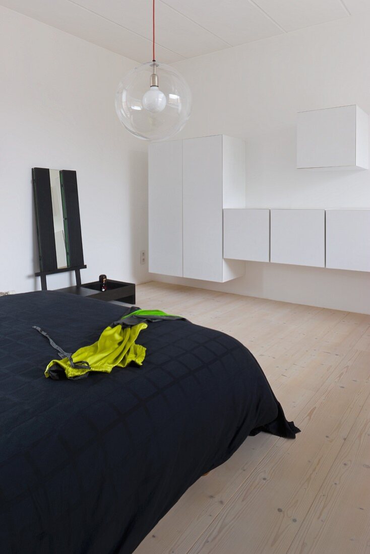 Double bed with a black coverlet and white floating cabinets in a minimalist bedroom