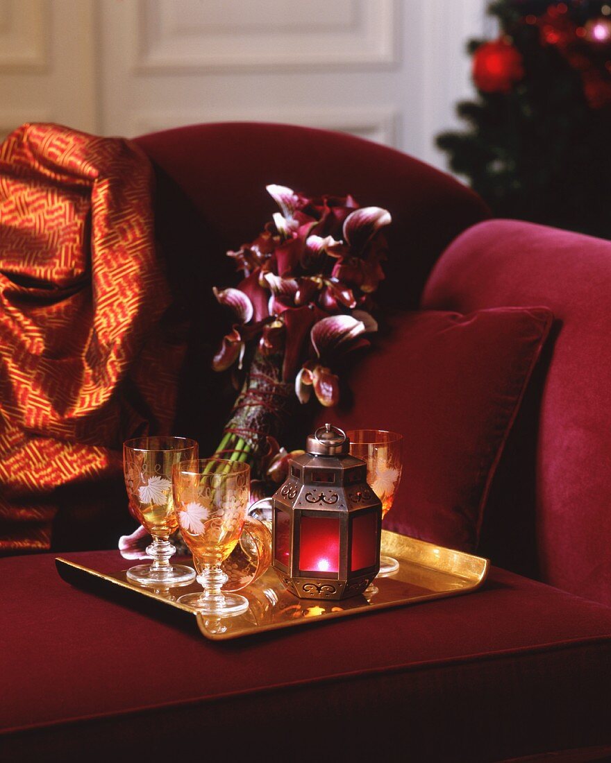Tablett mit Weingläsern, Windlicht und Orchideen auf rotem Sofa (weihnachtlich)
